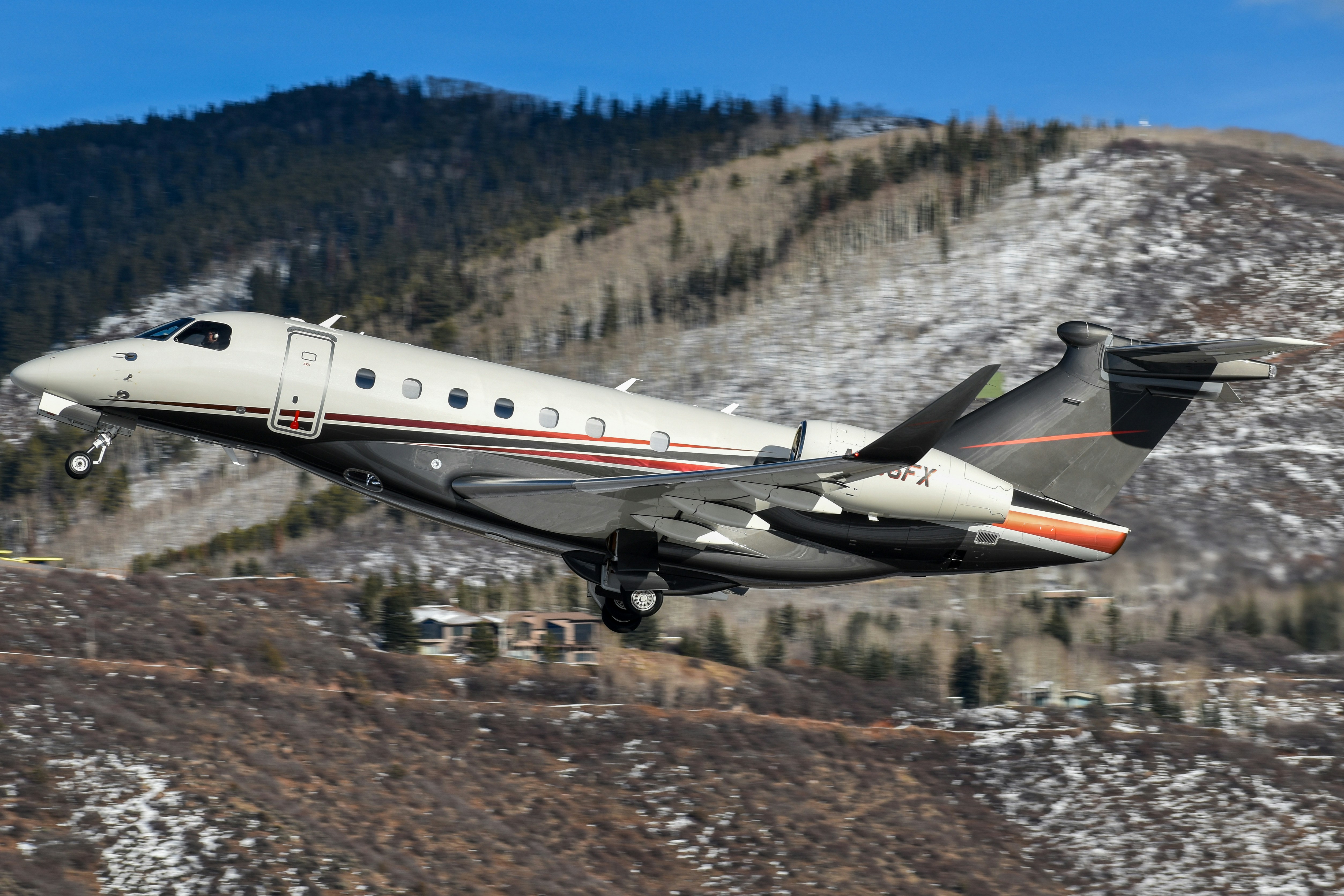 Sleek private jet ascending over snow-dusted mountains.