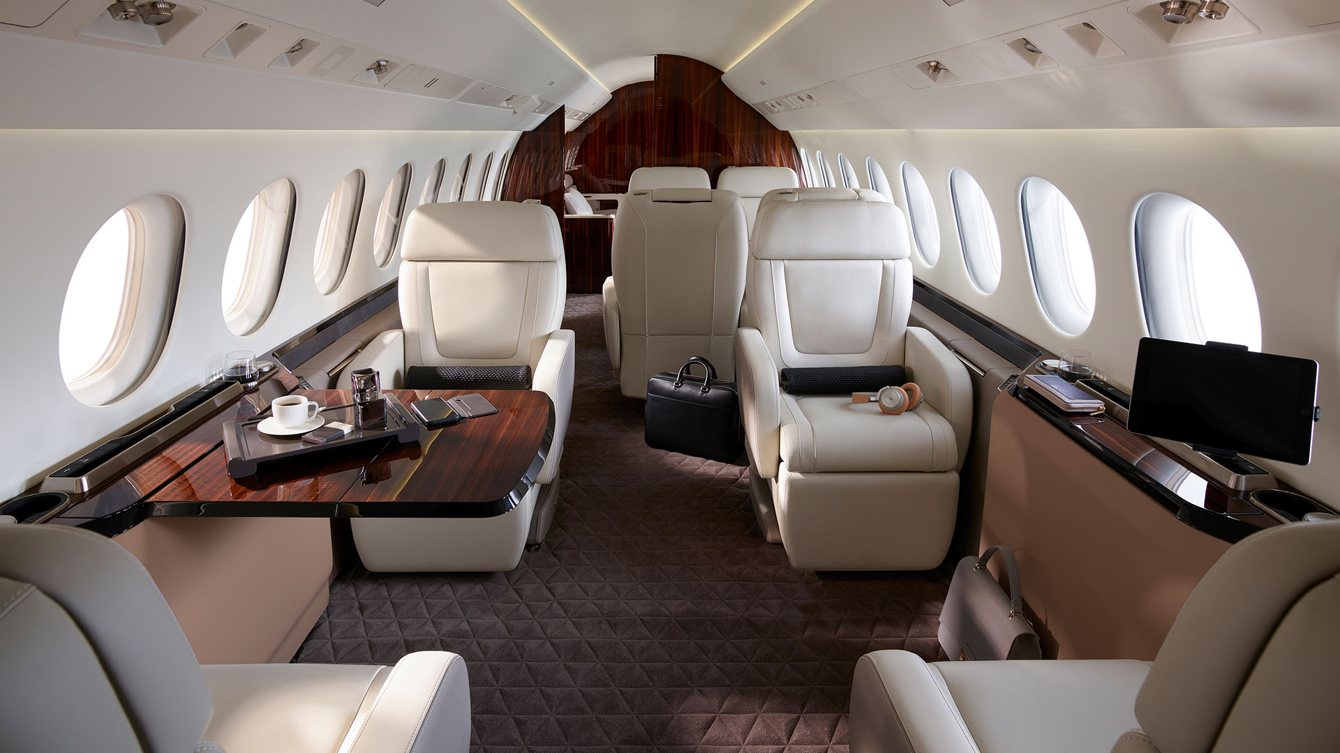 Luxurious private jet interior with white leather seats and wood-panelled tables.