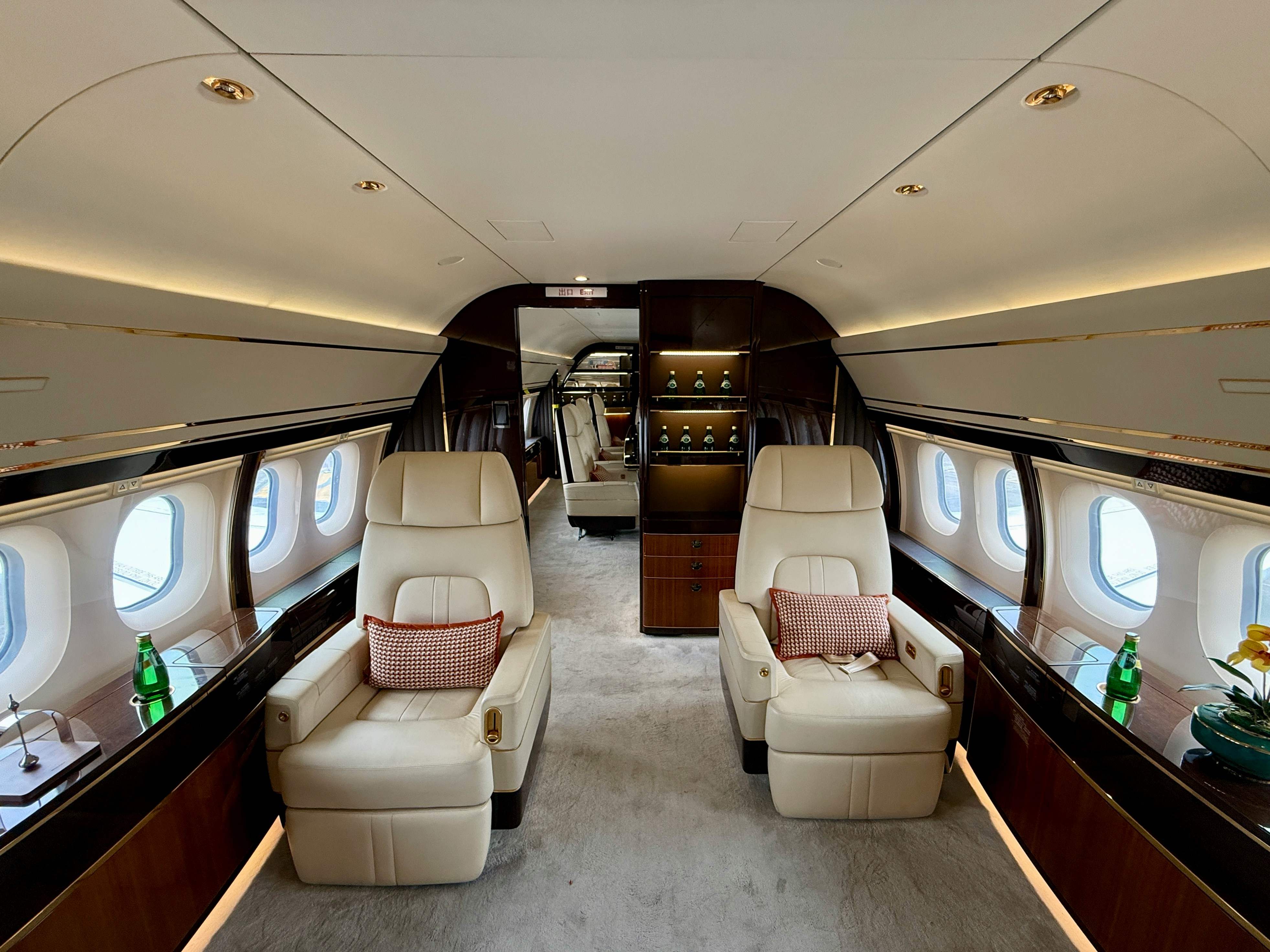 Luxurious private jet cabin with cream leather armchairs, patterned pillows, and warm ambient lighting.